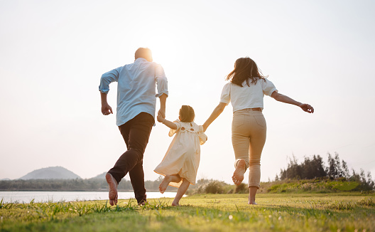 Happy family in the park sunset light. family on weekend running together in the meadow with river Parents hold the child hands.health life insurance plan concept.